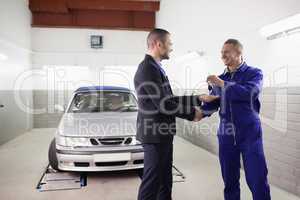 Mechanic giving car key while shaking hand to a client