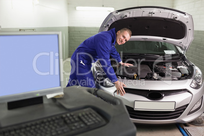 Mechanic leaning on a car next to a computer