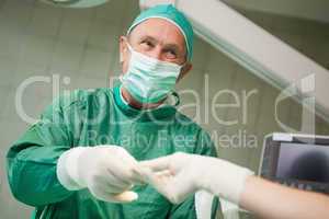 Smiling surgeon taking a tool from a gloved hand