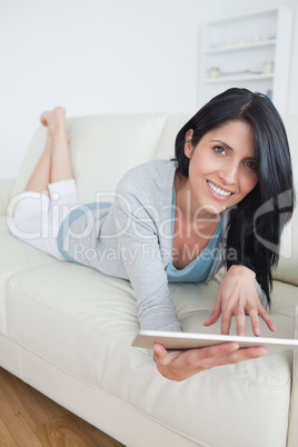 Smiling woman resting on a sofa while playing with a tablet