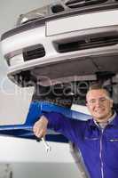 Smiling mechanic holding a spanner below a car