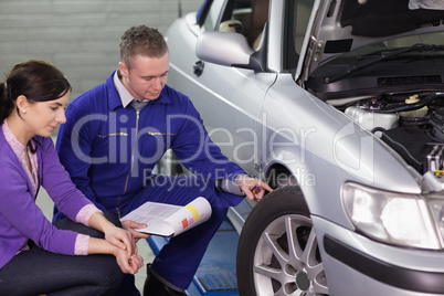 Mechanic touching the car wheel next to a client