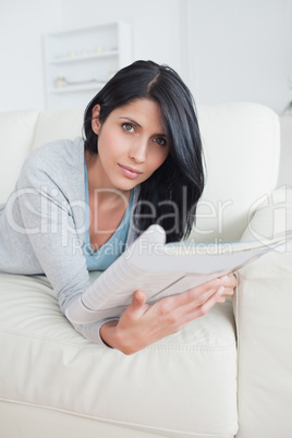 Woman laying on a couch as she holds a magazine