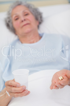 Patient holding drugs and plastic glass in her hands