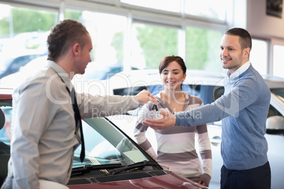 Smiling couple receiving keys from a car dealer