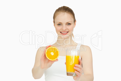 Cheerful woman presenting an orange while holding a glass