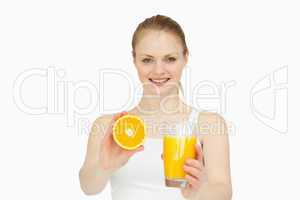 Cheerful woman presenting an orange while holding a glass