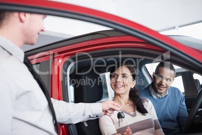 Couple sitting in a car receiving key from a car dealer