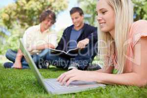 Girl using a laptop while lying in a park