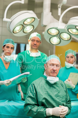 Surgeon sitting while crossing his hands with a team behind him