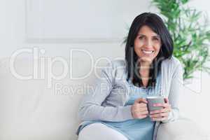 Smiling woman holding a mug with two hands while resting on a so