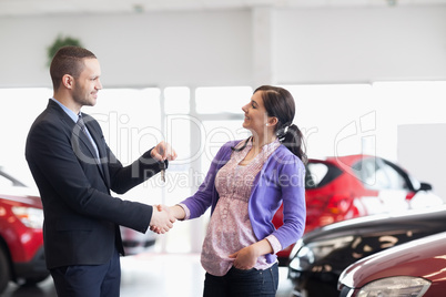 Salesman shaking the hand of a woman and giving her car keys