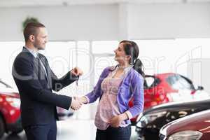 Salesman shaking the hand of a woman and giving her car keys