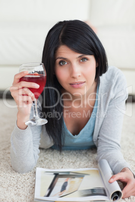 Woman lying on the floor while holding a glass of wine and a mag