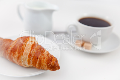 Croissant and a cup of coffee on white plates with sugar and mil