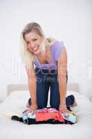 Smiling young woman trying to close her suitcase