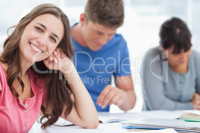 A smiling woman rests her head on her hand as she looks at the c