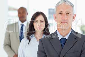 Mature and serious manager standing upright and followed by two