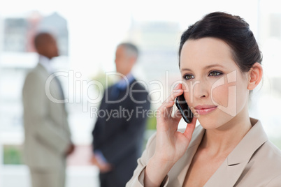 Young secretary using mobile phone in front of two businessmen