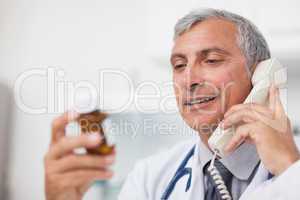 Doctor looking at a drug bottle while calling