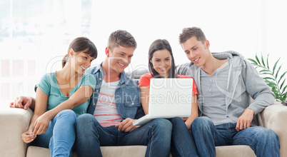 A smiling group of friends watching a show on the laptop togethe