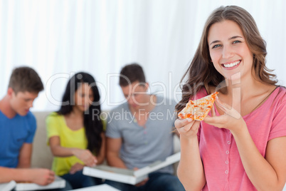 A smiling girl with a slice of pizza in front of her friends