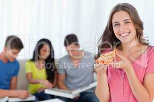 A smiling girl with a slice of pizza in front of her friends