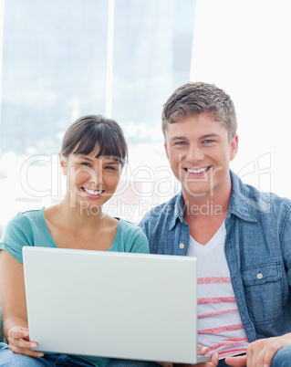 A smiling couple with a laptop as they look into the camera