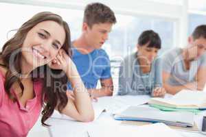 A girl smiling at the camera with her friends beside her studyin