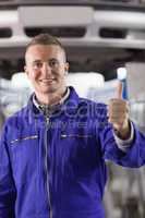 Mechanic standing with thumb up next to a car