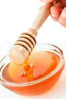 Honey dipper on the top of a bowl dropping honey