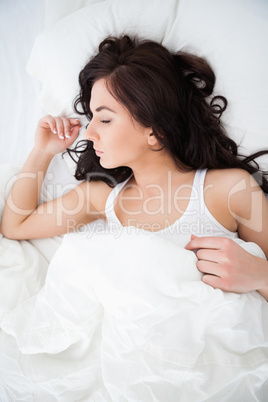 Brunette woman napping while lying under her quilt