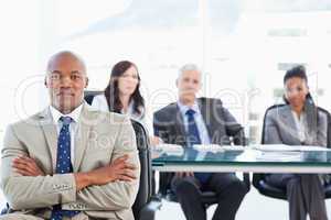 Young businessman crossing his arms with his team in the backgro