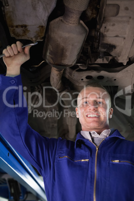Smiling mechanic looking at camera below a car