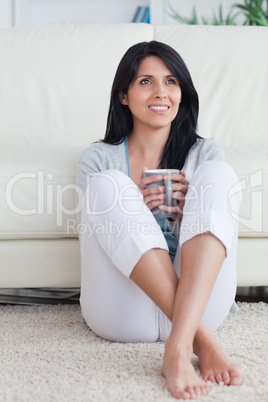 Woman sitting against a couch holding a mug