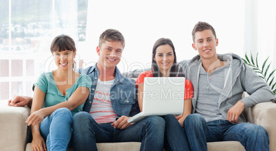 A group of friends sit on the couch with a laptop as they look a