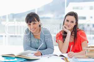 Two smiling students doing homework as they look into the camera