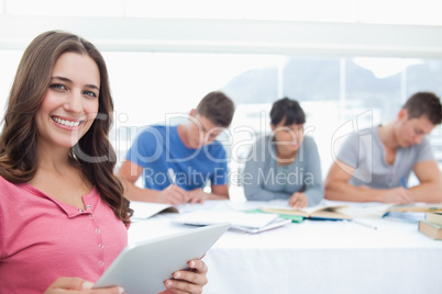 A smiling woman looking at the camera with a tablet in hand and