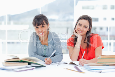 Two smiling students studying together while looking at the came