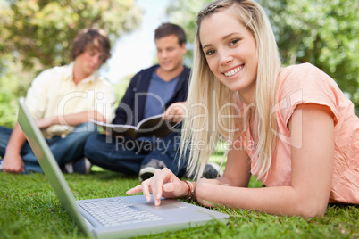 Portrait of a girl using a laptop while lying in a park