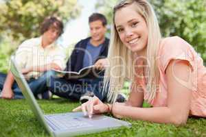 Portrait of a girl using a laptop while lying in a park