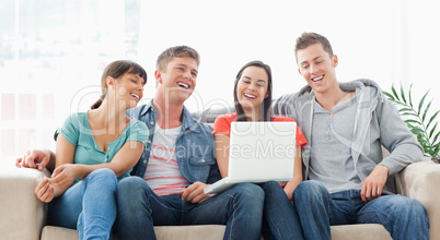 A laughing group sit together on the couch with a laptop watchin