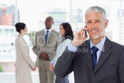 Smiling manager talking on the mobile phone while his team is be
