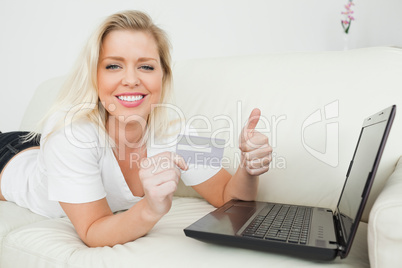 Woman with a thumb up and a credit card using a laptop
