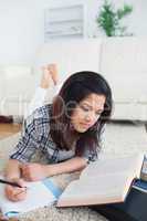 Woman reading a book while she writes on a notebook