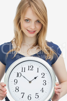 Woman holding a clock while looking at camera