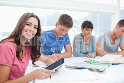 A girl looks into the camera with her tablet as her friends besi