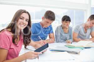 A girl looks into the camera with her tablet as her friends besi