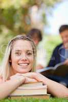 Close-up of a girl lying head on her books in a park