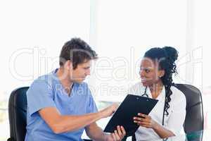 Young doctor showing something on a clipboard to his colleague